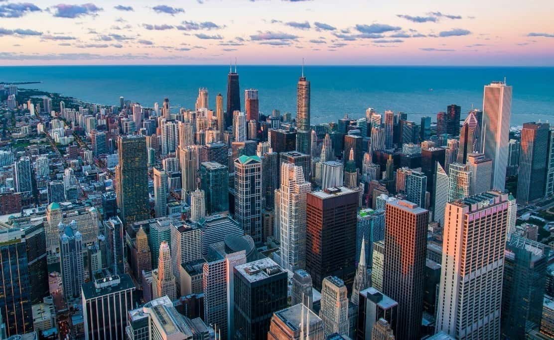 Aerial view of a city skyline with numerous skyscrapers along a large body of water under a cloudy sky.