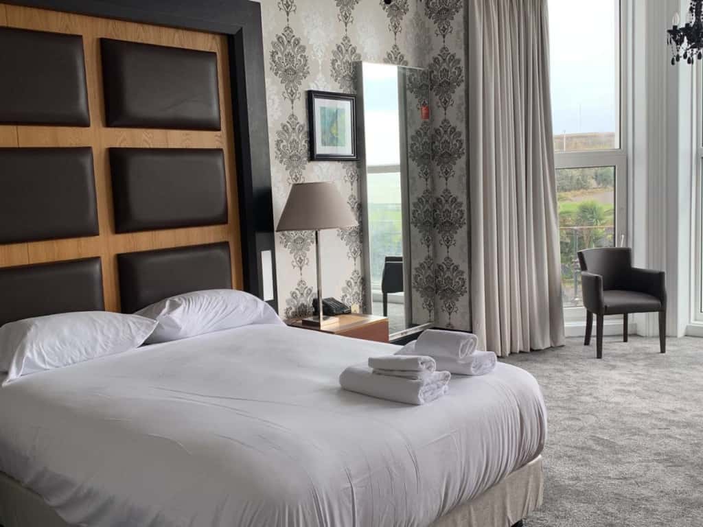 Hotel room with a large white bed, damask patterned wallpaper, and a window with light grey curtains