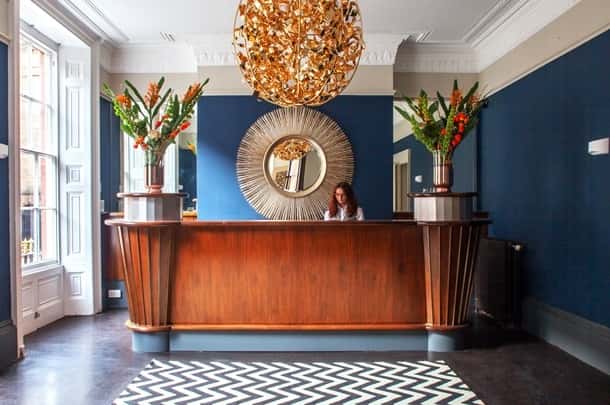 Reception desk with a woman, gold chandelier, and sunburst mirror in a lobby.