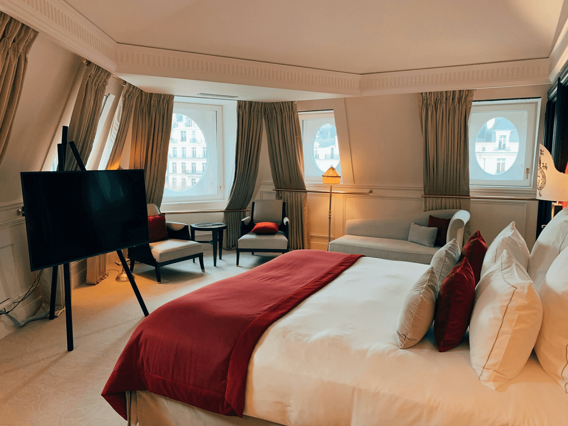 A hotel bedroom with a large bed, TV on an easel, two armchairs, a sofa, and round windows.