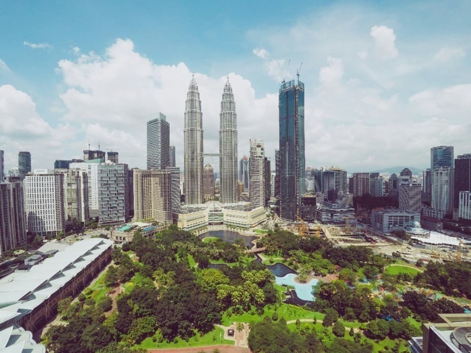 City skyline featuring two tall twin skyscrapers and a large green park with trees and a small lake under a blue sky