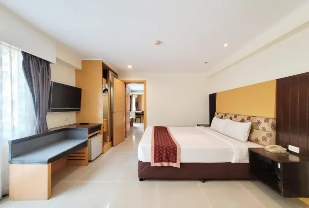 Hotel bedroom with a bed, wall-mounted TV, desk, wardrobe, and an open doorway.
