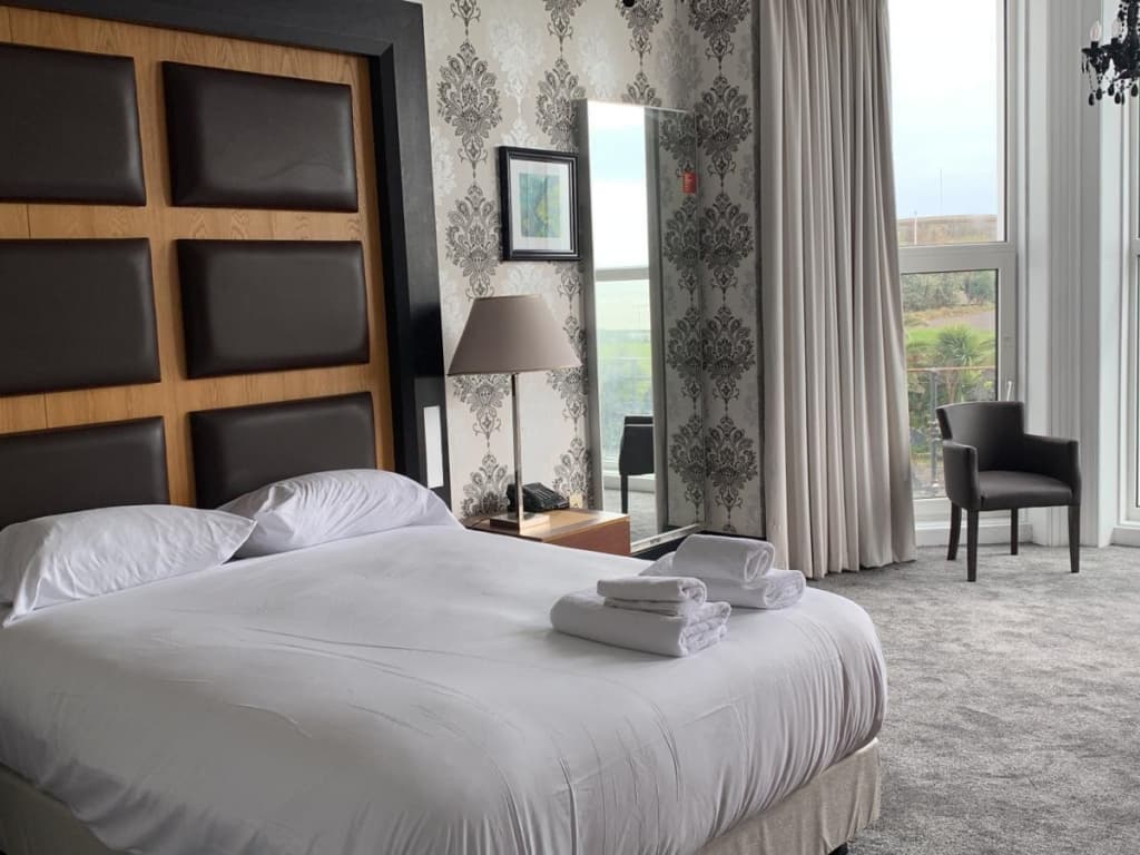 Hotel room with a large white bed, damask patterned wallpaper, and a window with light grey curtains