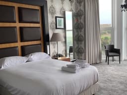 Hotel room with a large white bed, damask patterned wallpaper, and a window with light grey curtains