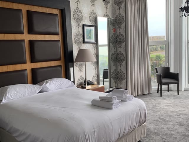 Hotel room with a large white bed, damask patterned wallpaper, and a window with light grey curtains