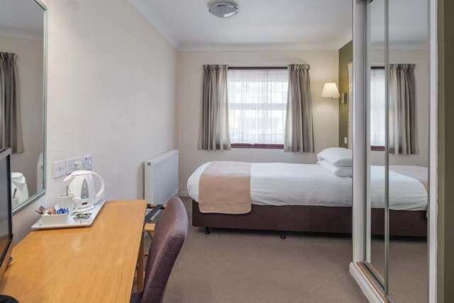 Hotel room featuring a single bed, a wooden desk with a kettle, and a large mirrored wardrobe.
