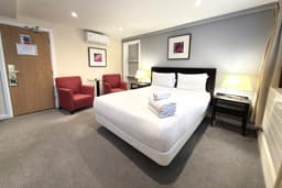 Hotel room with a white bed, folded towels, two red armchairs, and bedside lamps