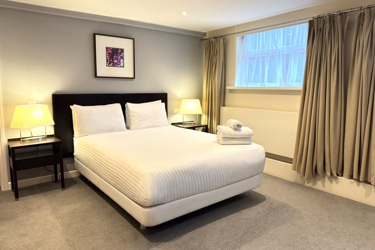 Hotel room with a double bed, folded towels, two bedside lamps, and curtained window