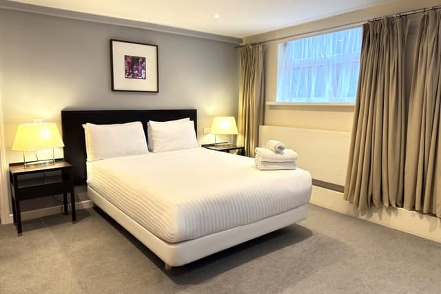 Hotel room with a double bed, folded towels, two bedside lamps, and curtained window