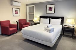 Hotel room with a white bed, folded towels, two red armchairs, and bedside lamps