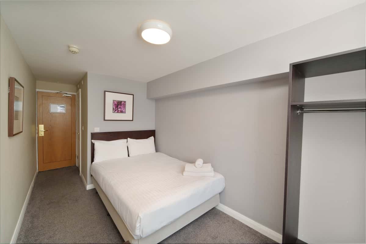 Hotel room with a made bed, folded towels, entry hallway, and open wardrobe