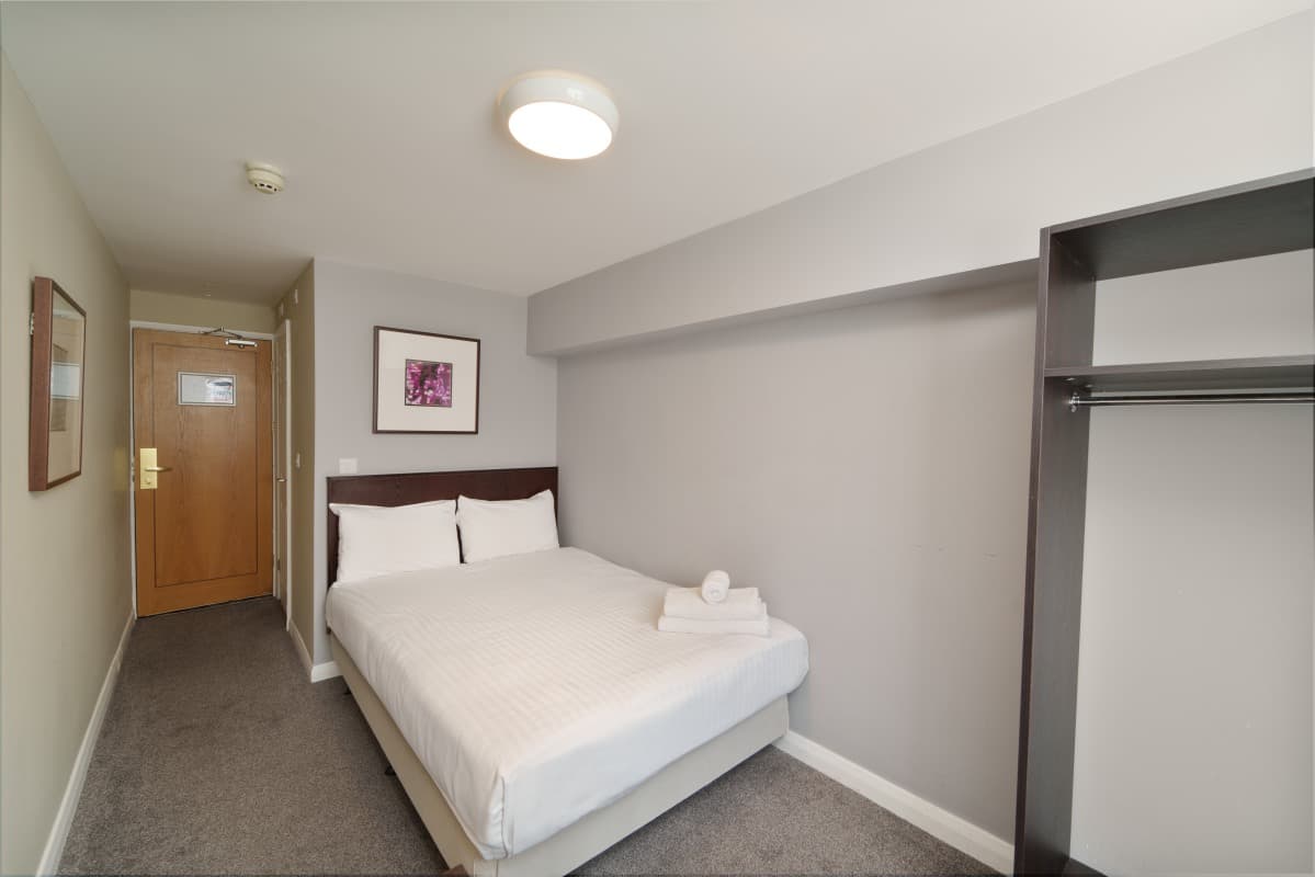 Hotel room with a made bed, folded towels, entry hallway, and open wardrobe