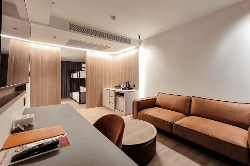Hotel room with brown leather sofa, round table, desk, and bunk beds visible in background