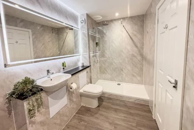 Bathroom with a walk-in shower, sink, toilet, and lit mirror on marble-tiled walls