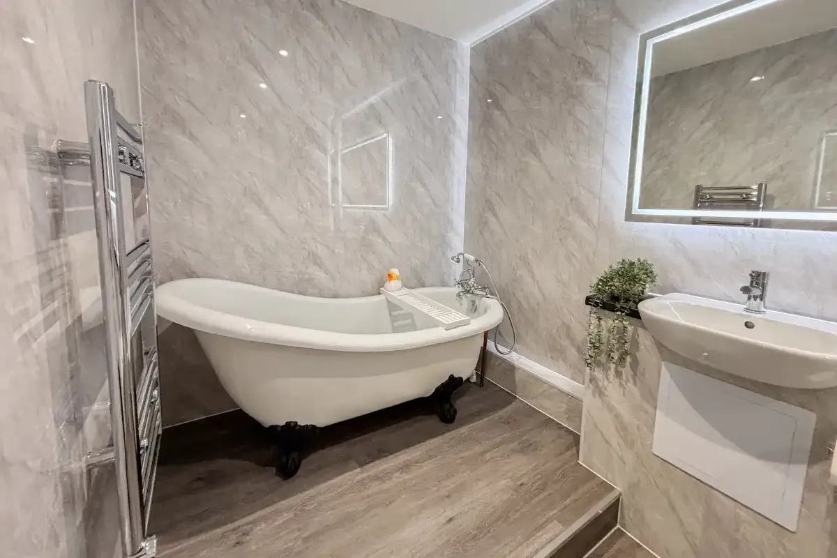 Freestanding clawfoot bathtub beside a wall-mounted sink and heated towel rail in a marble-tiled bathroom