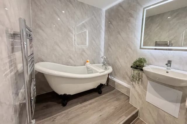 Freestanding clawfoot bathtub beside a wall-mounted sink and heated towel rail in a marble-tiled bathroom