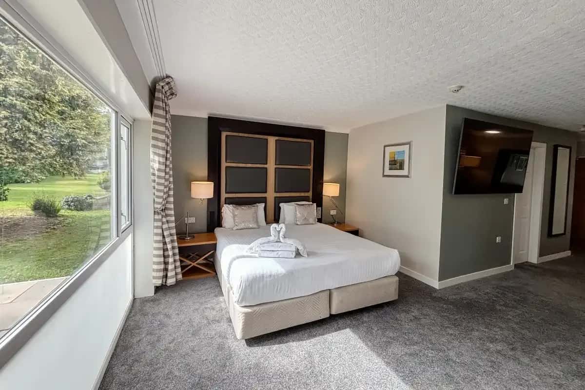 Hotel room with a double bed, wall-mounted TV, and large window overlooking a garden