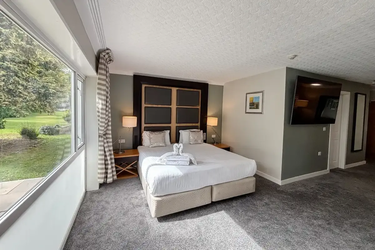 Hotel room with a double bed, wall-mounted TV, and large window overlooking a garden