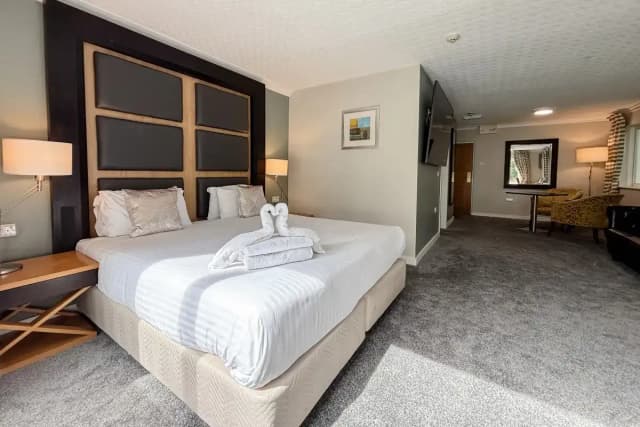 Hotel room with a large bed, folded towels shaped like swans, and a seating area beyond