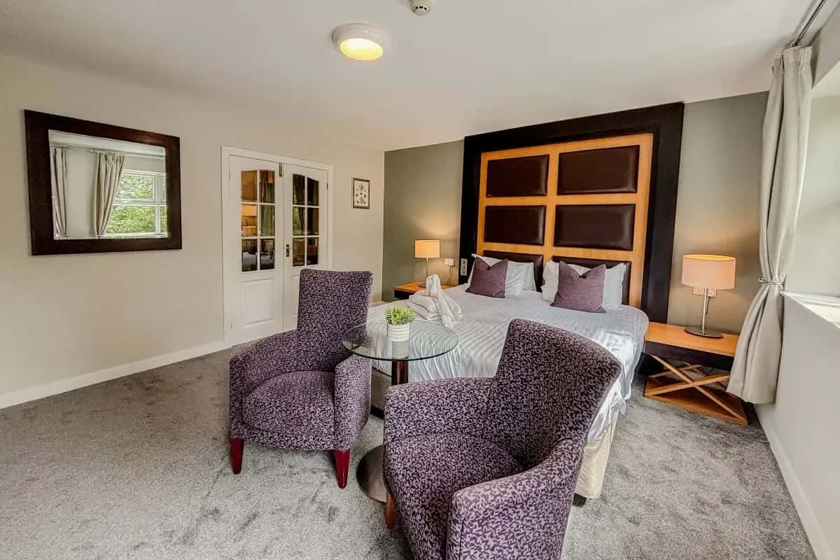 Hotel room with a bed, patterned armchairs, glass table, and French doors