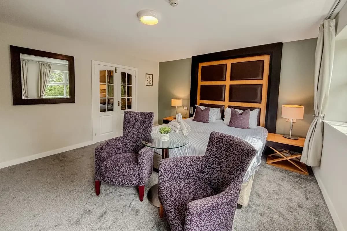 Hotel room with a bed, patterned armchairs, glass table, and French doors