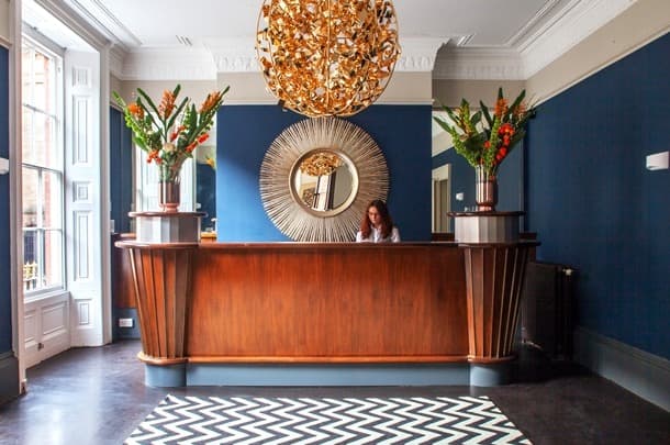 Reception desk with a woman, gold chandelier, and sunburst mirror in a lobby.