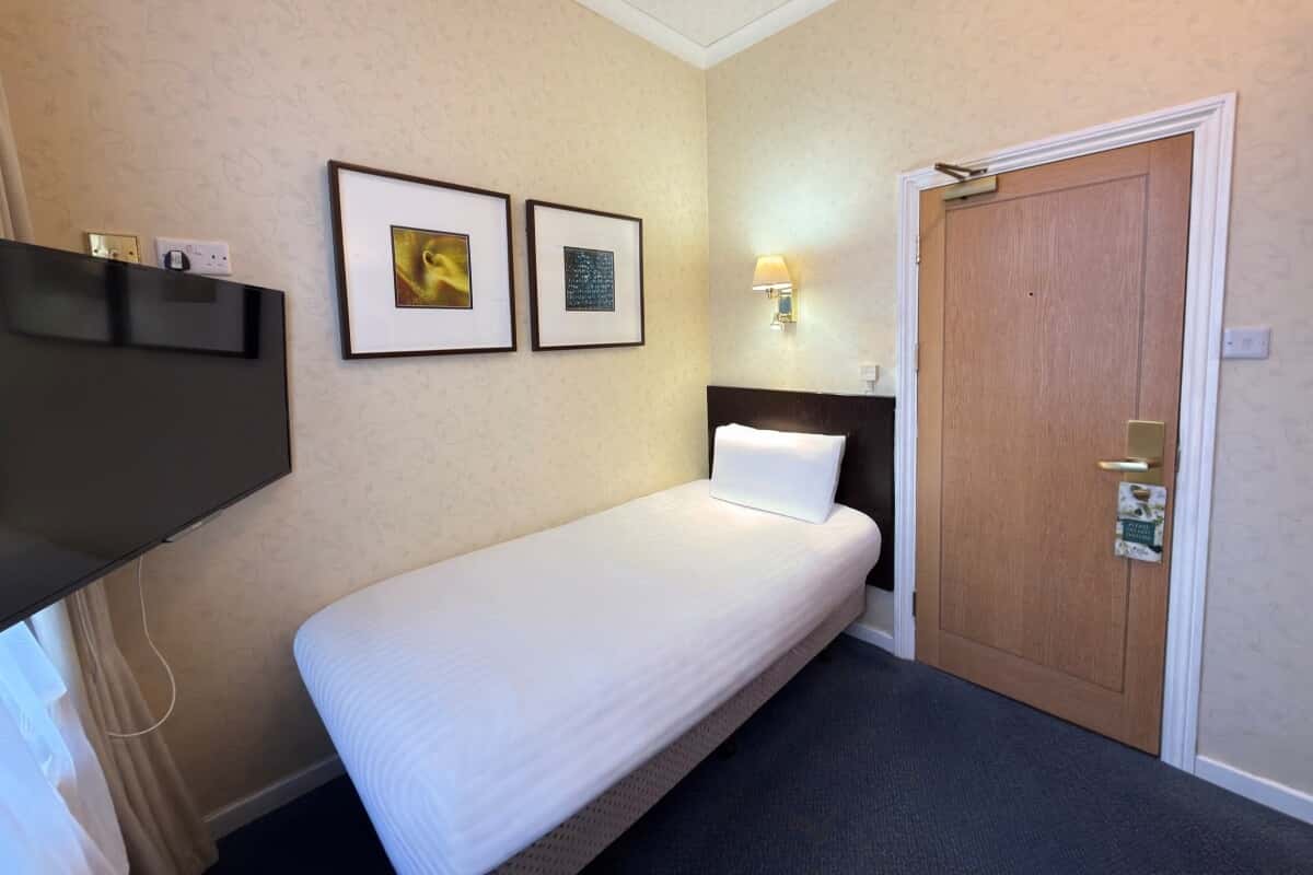 Single bed with white linens beside a wooden entrance door and wall-mounted television